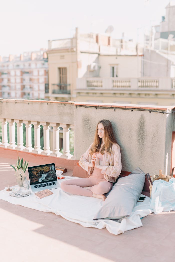 get-in-touch Caucasian woman practicing yoga with a laptop on a sunny balcony.